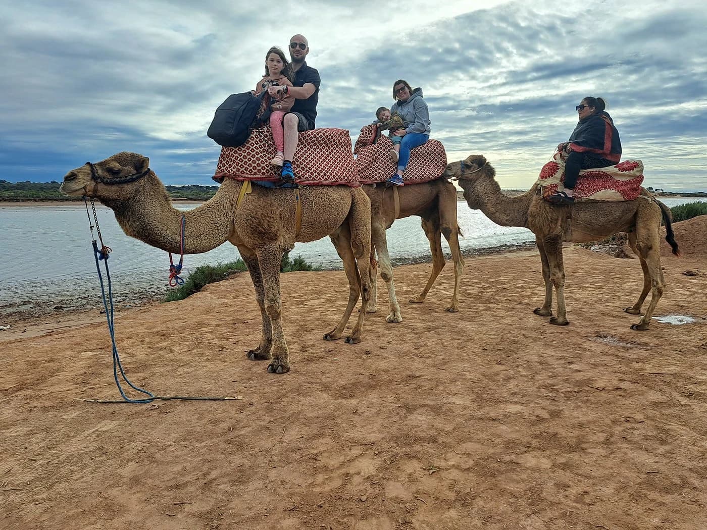 Riders on camels beside the Souss river under a cloudy sky