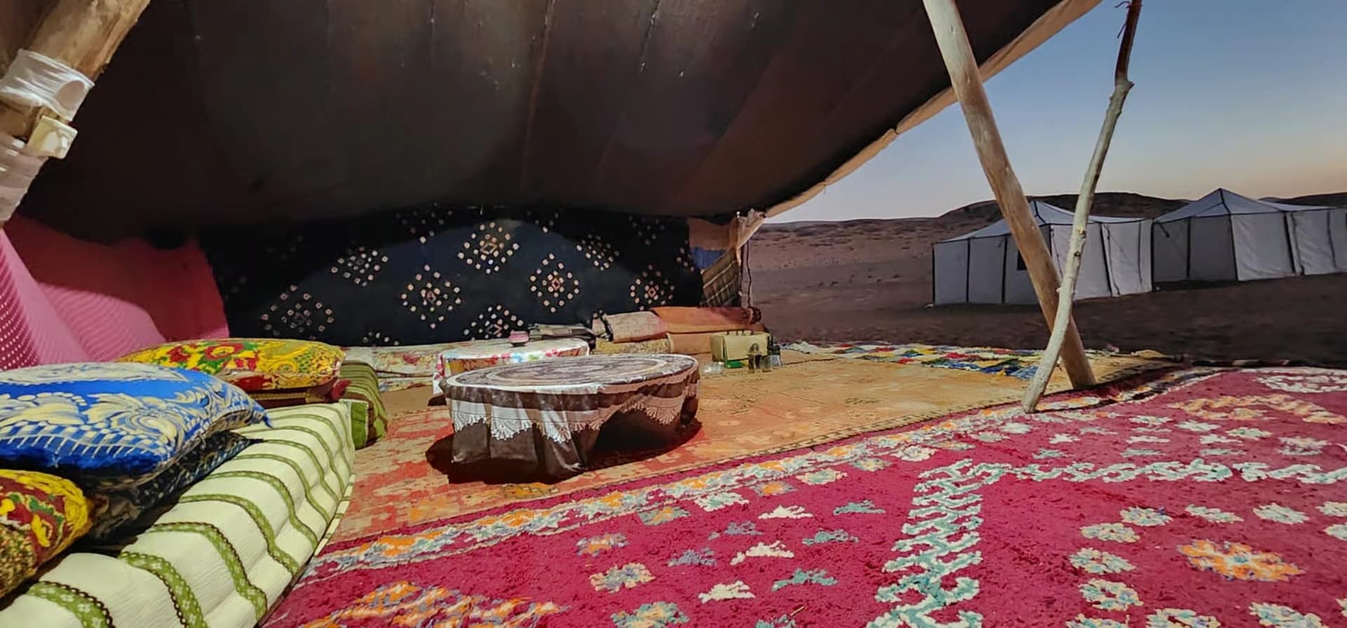 Cushioned seating under a canopy at the desert camp at dusk