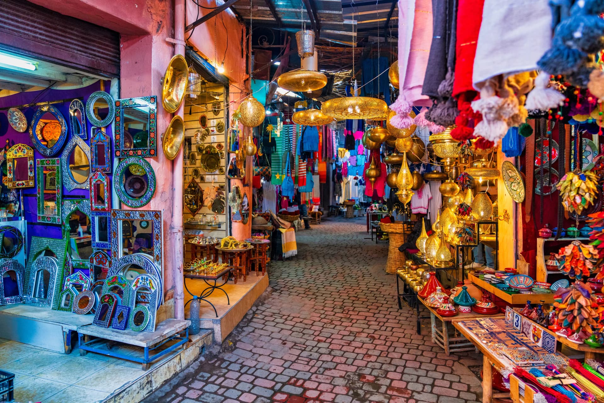 Souk stalls in the Marrakech medina hung with lanterns, mirrors, tagines and leather bags