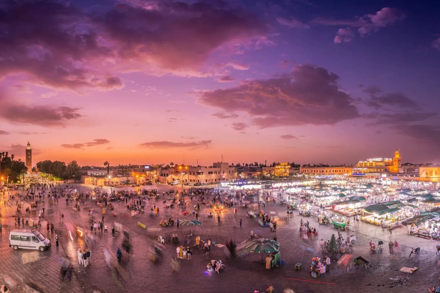 Jemaa el-Fnaa square at dusk with food stalls lit up and the Koutoubia minaret on the horizon