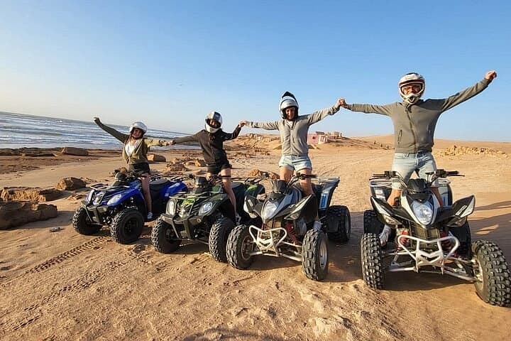 Four riders in helmets standing beside their quads on the beach