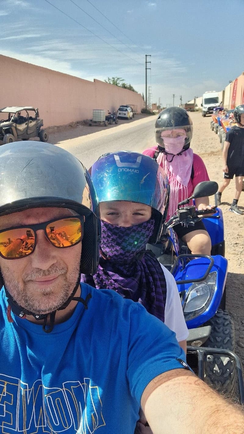Selfie of a man with two helmeted children on blue quads by a village road