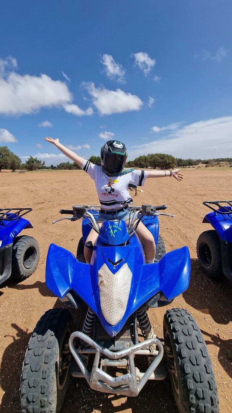 A helmeted rider with arms outstretched sitting on a blue quad