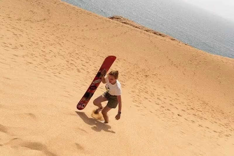 Man carrying a red sandboard up the dune